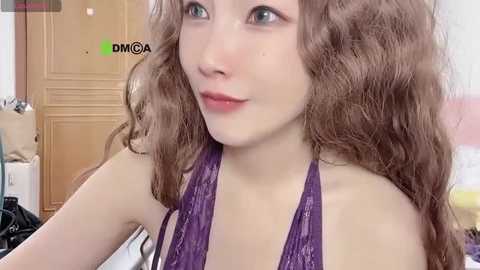 Media: A video of a young woman with fair skin and wavy, light brown hair, wearing a purple lace bralette, looking to the side in a casual, indoor setting with wooden furniture and a green DMCA watermark in the corner.