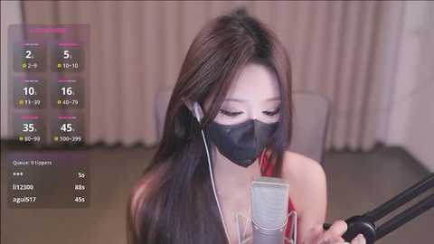 Media: Video of an Asian woman wearing a black face mask, headphones, and a red top, reading from a script on a microphone stand, in a beige room.