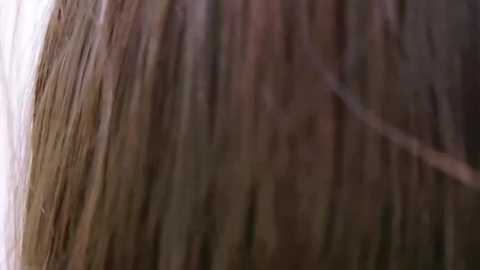 Media: Close-up video of a man's shoulder-length brown hair, featuring natural highlights and slight waves, seen from a side angle. The background is blurred, focusing attention on the texture and color of the hair.