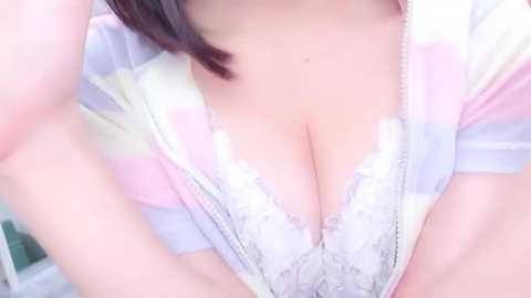 Media: Video of a woman's cleavage, wearing a white lace bra under a pastel striped top, with pale skin and dark hair partially visible.