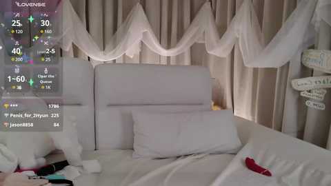 Media: A video of a serene, white bedroom with a canopy bed draped in sheer white fabric, featuring a plush white pillow and a red vibrator on the bed.