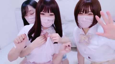 Media: Video of three Asian women with long black hair, wearing white school uniforms, masks, and name tags, posing and smiling.