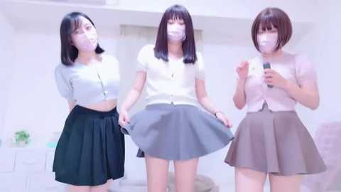 Media: Video of three young East Asian women wearing face masks and school uniforms, smiling and posing in a bright, modern room.