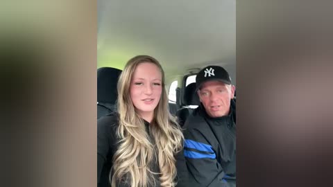 Media: Video of a blonde woman with long hair, wearing a black top, seated in a car beside an older man in a black Yankees cap.