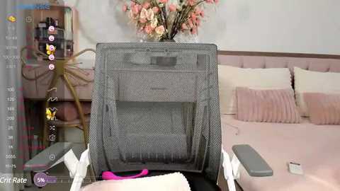 Media: Video of a gray, mesh baby swing with a white base, positioned in a modern, light pink nursery with plush pillows, a floral arrangement, and a white nightstand.