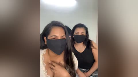 Media: Video of two women wearing black face masks, one with long black hair, the other with short hair, smiling, indoors, blurred background.