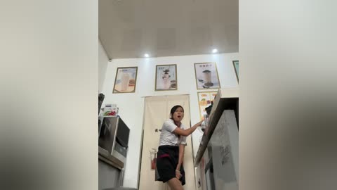 Media: A video of a woman in a white shirt and black skirt, animatedly gesturing with a hand, in a modern kitchen with white walls, recessed lighting, and framed posters.