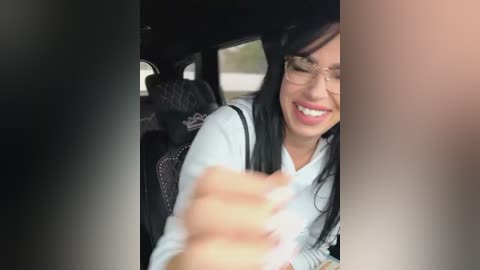 Media: Video of an Asian woman with long black hair, wearing glasses, white shirt, and black backpack, laughing in a car seat, with blurred passengers visible.