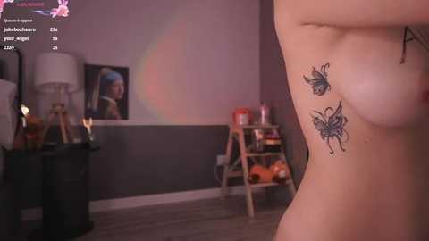 Media: A video shows a nude woman with a tattoo of two butterflies on her side, standing in a dimly lit room with a bed, a lamp, and a wooden shelf in the background.