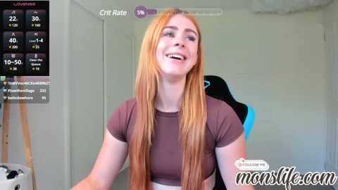 Media: Video of a smiling, fair-skinned woman with long, straight red hair, wearing a brown crop top, sitting on a black gaming chair in a room.