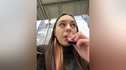 Media: A video of a young woman with straight, long brown hair, wearing a black sweater, brushing her teeth inside a modern, industrial bathroom with metal fixtures and a metallic ceiling.