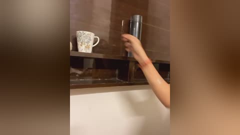 Media: Video of a person with a fair complexion, wearing a white shirt, reaching for a metal canister on a dark wooden shelf above a white countertop in a kitchen.