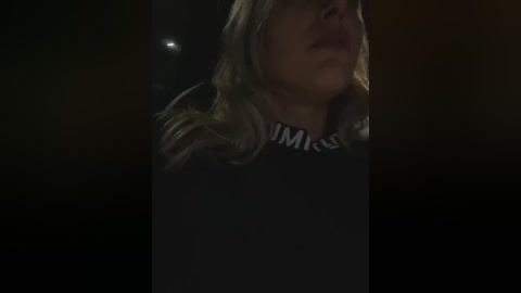 Media: A dimly lit video shows a close-up of a woman with blonde hair and glasses, wearing a black shirt with white lettering. Her face is partially visible, suggesting a contemplative or distressed expression.