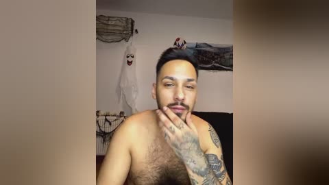 Media: Video of a shirtless, tanned, tattooed Hispanic man with short black hair, holding his fingers to his lips, surrounded by Halloween decorations.