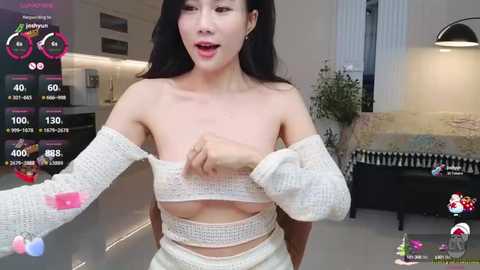 Media: Video of an Asian woman with long black hair, fair skin, and medium breasts, wearing a white knit top pulled down to reveal her chest, in a modern bedroom.