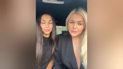 Media: Video of two women with long hair, one with dark brown hair, the other with blonde hair, both wearing black tops, smiling, sitting closely in a car.