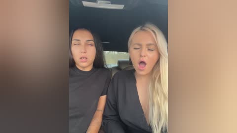 Media: Video of two young women, one with long black hair, the other with long blonde hair, both in black tops, sitting close in a car, eyes closed, mouths open, suggesting intimacy.