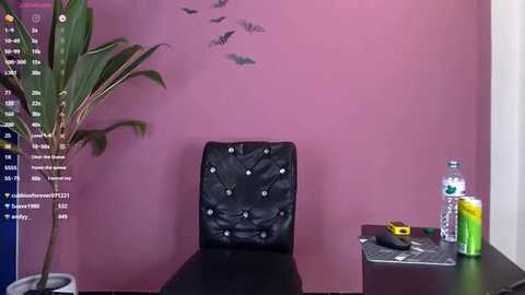 Media: Video of a minimalist office corner with a black, tufted leather chair, a potted plant, a water bottle, and a yellow notepad on a dark desk against a mauve wall.