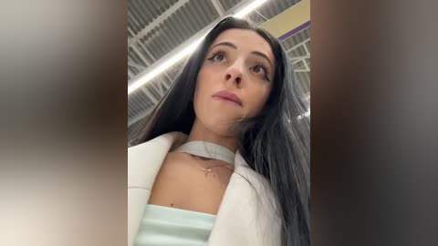 Media: A video of a young woman with long black hair, fair skin, and a light blue top, taken from a low angle, indoors with a ceiling and lighting visible.