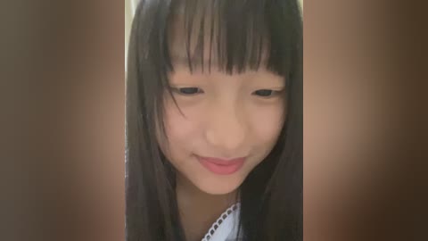 Media: A close-up video of a young Asian girl with long black hair and bangs, wearing a white dress with black polka dots. She has a gentle smile and a soft, smooth complexion. The background is blurred in a warm, neutral tone.