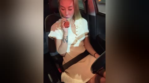 Media: Video of a blonde woman with fair skin, wearing a white blouse and beige skirt, drinking from a red can in a car seat.