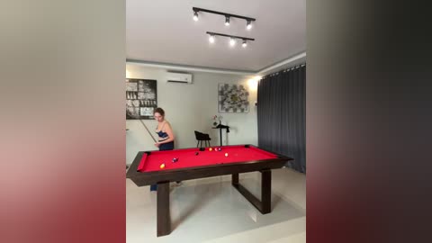 Media: Video of a modern room with a pool table, a woman wearing a blue top and shorts, and a black chair in the background.