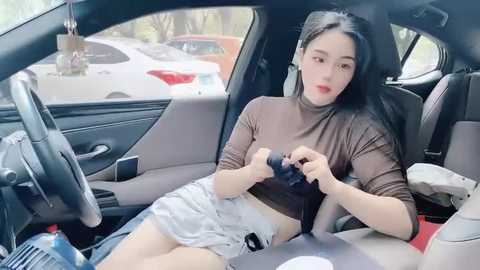 Media: Video of an East Asian woman with long black hair, wearing a brown turtleneck and short white skirt, adjusting a camera in a car.