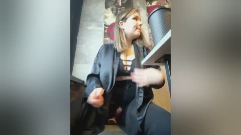 Media: A video of a young woman with blonde hair, wearing a black leather jacket and a black lace bra, sitting on a chair in an office. She appears to be using a laptop.