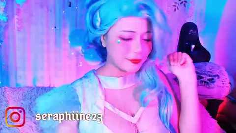 Media: Video of a pale-skinned woman with long, wavy blue hair, wearing a white corset and red lipstick, making a hand gesture against a blue and purple backdrop.