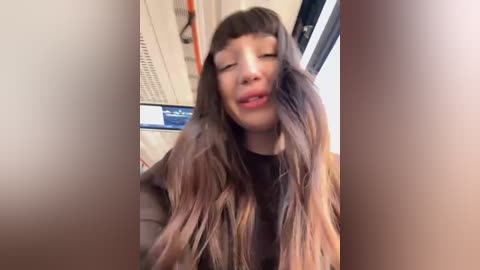 Media: A video of a woman with long, straight, dark brown hair styled in a blunt bang, wearing a black top, inside a train, with blurred background.