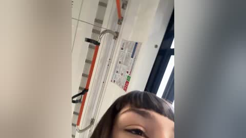 Media: A video of a woman with straight brown hair, looking down, taken from a low angle. She is in a bathroom with white walls, a window, and a tiled shower area. The image has a slight blur.