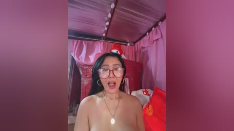 Media: A video of an Asian woman with long black hair, glasses, and a shocked expression, topless, standing in a pink room with red curtains and a red stuffed toy.