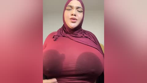 Media: A video of a curvaceous woman with large breasts wearing a maroon hijab and long-sleeved top, her nipples clearly visible through the fabric, with a blurred background.