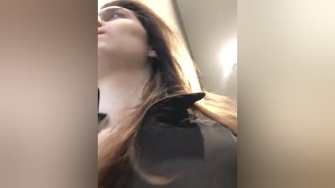 Media: A video of a young woman with light skin and long brown hair, wearing a black top, viewed from the side in a dimly lit hallway.