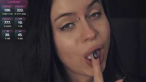 Media: A video shows a young woman with pale skin and long, dark hair, biting her nail, with a nose ring, and black eyeliner. The background is dark, and a digital display shows 100% humidity and 72.2\u00b0F.