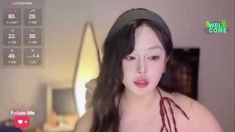 Media: Video of a young Asian woman with long black hair, wearing a black headband, red halter top, and red lipstick, in a dimly lit room.