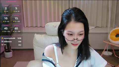 Media: A video of an East Asian woman with long black hair, wearing glasses, a white sailor collar shirt, and sitting on a white couch.