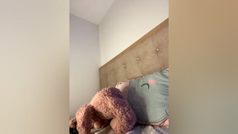 Media: A video of a cozy bedroom corner with a plush teddy bear and a stuffed elephant on a bed with a beige tufted headboard, beige pillows, and a soft, light-colored blanket.