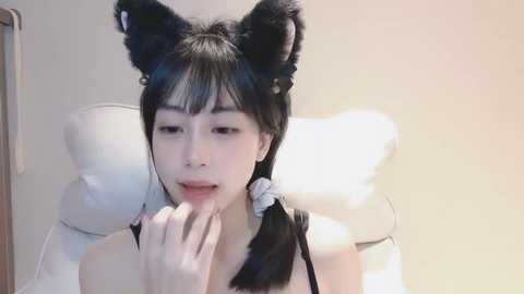 Media: Video of an East Asian woman with black hair, wearing black cat ears and a black dress, seductively licking her fingers in a bedroom setting.