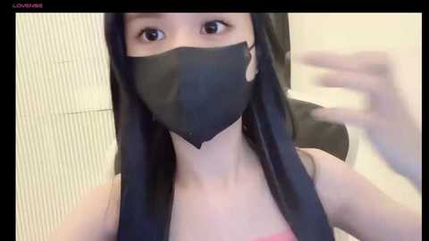 Media: Video of an Asian woman with long black hair, wearing a black face mask, pink tank top, and standing in a tiled bathroom.