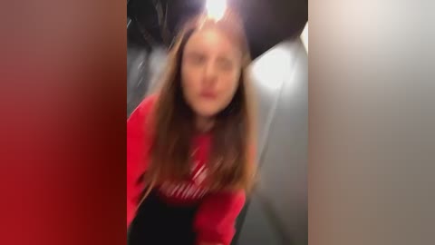 Media: A blurred video of a young woman with long brown hair, wearing a red sweater, standing in a dimly lit, metallic room.