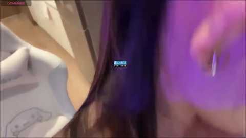 Media: Video of a close-up, blurred face with purple makeup, wearing a white mask with the word \"REDS\" in the center. Background features a white bed and beige floor, suggesting a bedroom setting.