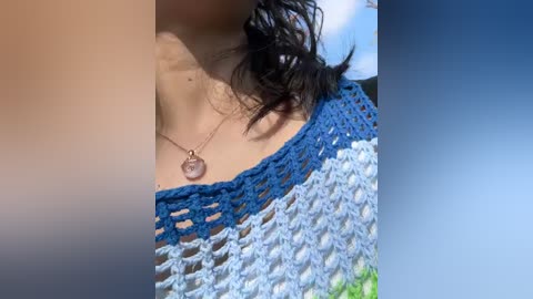 Media: Video of a close-up of a woman's neck and chest, wearing a blue and white crochet top with a delicate silver necklace featuring a heart pendant.