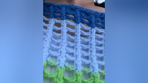 Media: Video of a handmade, crocheted blanket featuring vibrant stripes in blue, white, and green, with a textured, knitted pattern. The blanket is laid out on a light-colored surface, possibly a bed or sofa.