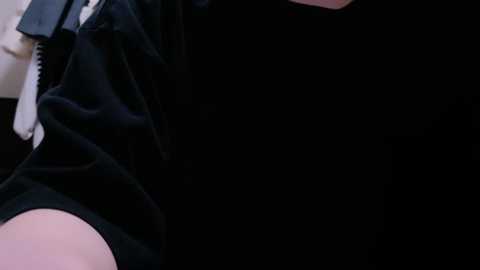 Media: Video of a person's upper body in black clothing against a dark background. The image is cropped, focusing on the torso and shoulders. The fabric appears smooth and the lighting is dim.