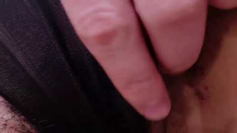 Media: Video of a close-up view of a hand pressing against a light brown skin, with a darker cloth visible in the background. The image is intimate and detailed.