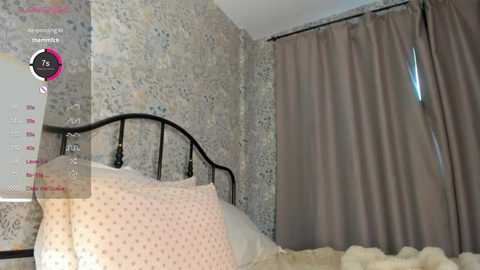 Media: Video of a vintage-style bedroom with floral wallpaper, a black metal bed, pink polka-dot pillows, beige curtains, and a white ceiling.