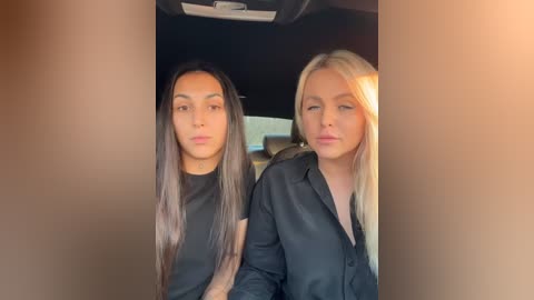 Media: Video of two women in black shirts, seated in a car, with the car's interior visible. The woman on the left has long, straight, dark hair, while the woman on the right has long, straight, blonde hair.