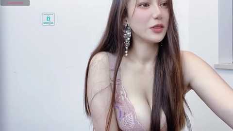 Media: Video of an East Asian woman with long, straight, dark brown hair, wearing a light pink lace bra, silver dangling earrings, and makeup, against a plain white background.