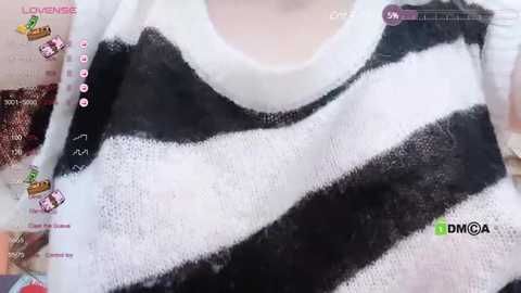 Media: A close-up video of a white and black striped sweater, worn by a person with fair skin. The sweater has a soft texture, and the background shows a blurred, colorful fabric.